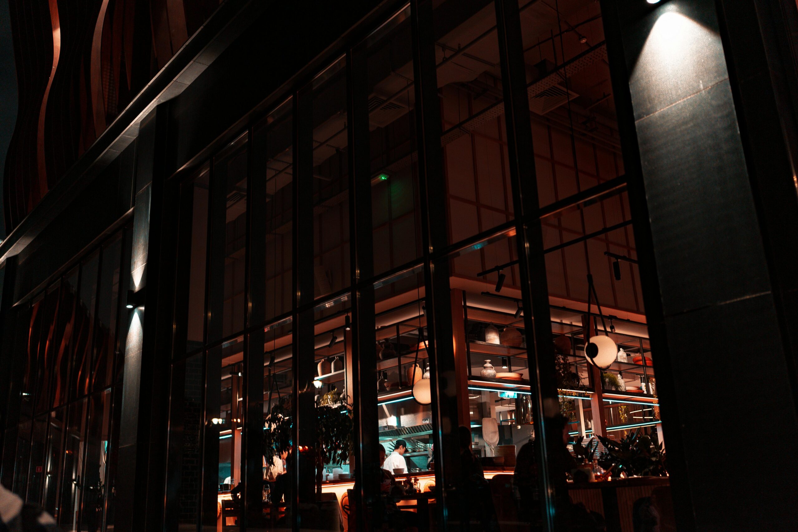 Exterior view of a stylish urban restaurant at night with visible interior lighting and decor.